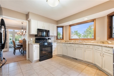 Kitchen with black appliances, white cabinets, light tile patterned floors, light stone counters, and a chandelier
