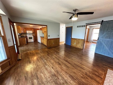 Unfurnished living room with a barn door, wainscoting, ceiling fan, wood walls, and a textured ceiling