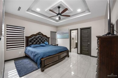 Bedroom featuring a raised ceiling, baseboards, ceiling fan, recessed lighting, and ensuite bath