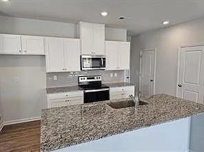 Kitchen featuring recessed lighting, appliances with stainless steel finishes, white cabinetry, light stone countertops, and dark wood-type flooring