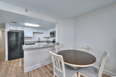 Kitchen featuring appliances with stainless steel finishes, white cabinetry, light stone counters, light wood-type flooring, and a peninsula