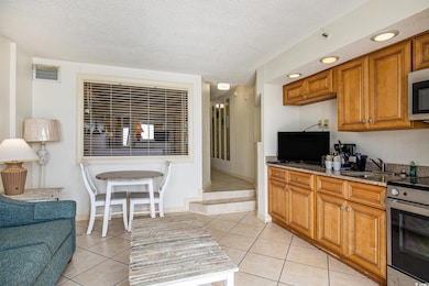 Kitchen featuring brown cabinetry, light stone counters, stainless steel appliances, light tile patterned flooring, and a textured ceiling