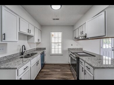 Kitchen featuring stainless steel appliances, a sink, dark wood-style flooring, white cabinetry, and light stone countertops