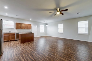 Kitchen with brown cabinets, open floor plan, dark wood finished floors, a kitchen island, and appliances with stainless steel finishes