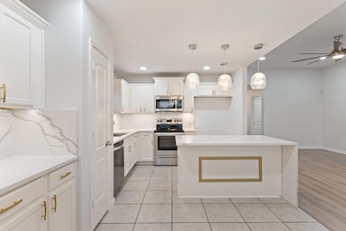 Kitchen featuring a kitchen island, ceiling fan, white cabinets, light tile floors, and appliances with stainless steel finishes