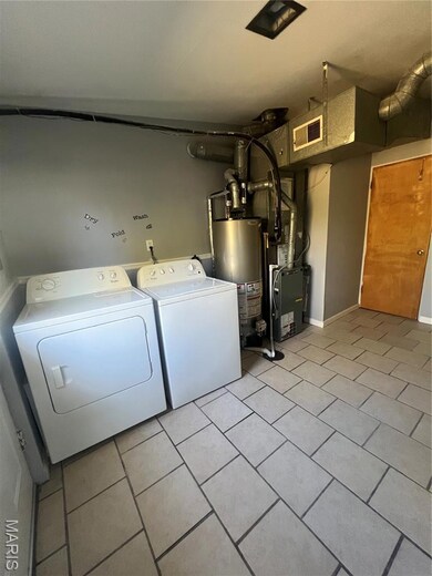 Laundry room featuring light tile patterned flooring, washing machine and dryer, and water heater