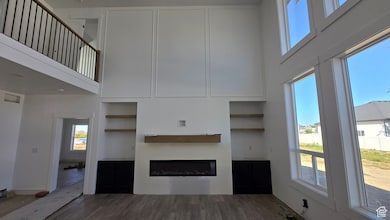 Unfurnished living room featuring dark wood finished floors, a towering ceiling, and a glass covered fireplace
