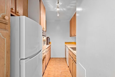 Kitchen featuring white appliances, light countertops, light tile patterned floors, and brown cabinets
