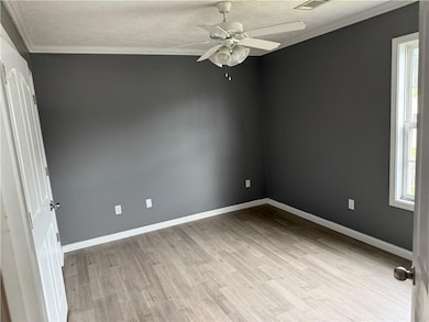 Empty room with wood finished floors, ceiling fan, a textured ceiling, and crown molding