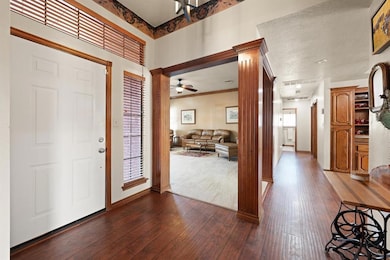 Entrance foyer with dark wood-style flooring, ceiling fan, ornate columns, and crown molding