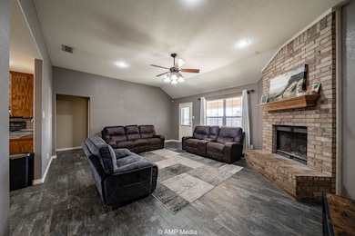 Living room with vaulted ceiling, a textured ceiling, a ceiling fan, a brick fireplace, and dark wood-style flooring