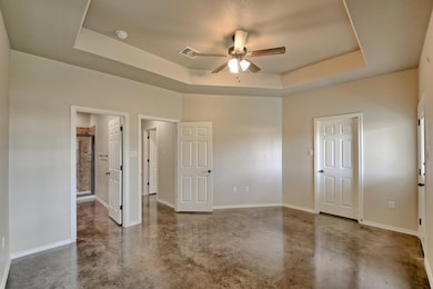 Unfurnished bedroom featuring a raised ceiling, finished concrete flooring, and ceiling fan