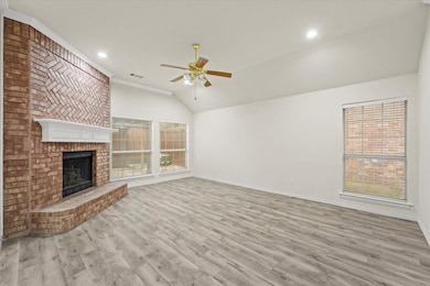 Unfurnished living room featuring light wood-type flooring, vaulted ceiling, a brick fireplace, a ceiling fan, and crown molding