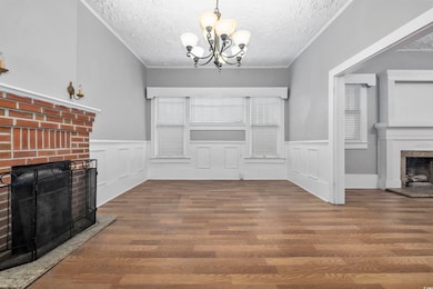 Unfurnished living room with a textured ceiling, a chandelier, dark wood-type flooring, and a brick fireplace