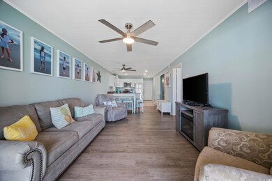 Living room featuring wood finished floors, a ceiling fan, ornamental molding, and a fireplace