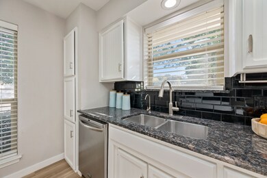 Kitchen with tasteful backsplash, dark stone counters, stainless steel dishwasher, white cabinetry, and light wood-style floors
