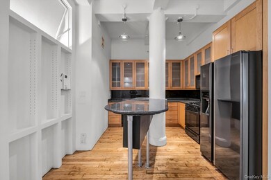 Kitchen featuring black appliances, hanging light fixtures, light wood-style floors, dark stone countertops, and glass insert cabinets
