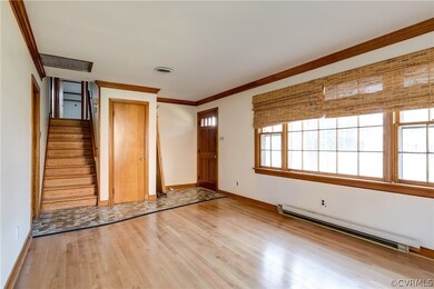Entry way has tile floor and coat closet, opens into large living room with hardwood floors, crown molding, and beautiful picture window. Steps in center lead to second floor bedrooms.