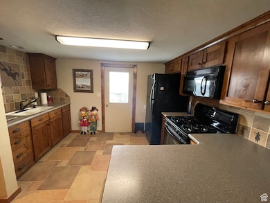 Kitchen with a textured ceiling, black appliances, a sink, and decorative backsplash