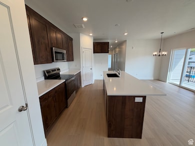 Kitchen with appliances with stainless steel finishes, dark brown cabinetry, light wood-style floors, recessed lighting, and a kitchen island with sink