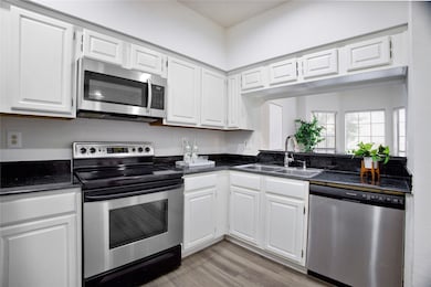 Kitchen with stainless steel appliances, white cabinets, light wood-type flooring, and dark stone countertops