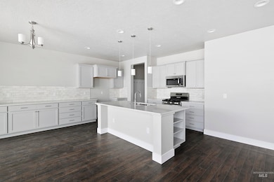 Kitchen with white cabinetry, an island with sink, appliances with stainless steel finishes, decorative backsplash, and hanging light fixtures
