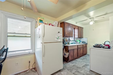Kitchen featuring a ceiling fan, washer / clothes dryer, freestanding refrigerator, light countertops, and dark brown cabinets