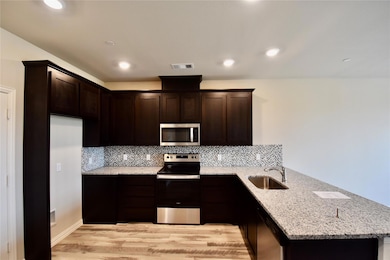 Kitchen featuring tasteful backsplash, light hardwood / wood-style flooring, stainless steel appliances, sink, and light stone countertops