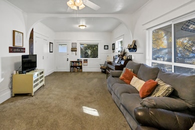 Living room featuring carpet, ceiling fan, arched walkways, and ornamental molding