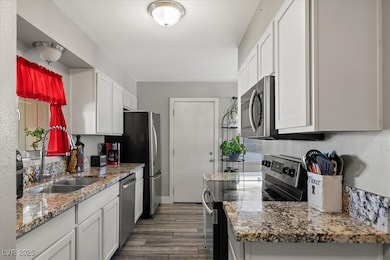 Kitchen with stainless steel appliances, light stone counters, dark wood-style flooring, and white cabinets