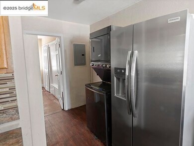 Kitchen with stainless steel fridge with ice dispenser, dark wood-style floors, stacked washer / drying machine, and electric panel