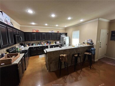 Kitchen with dark cabinets, crown molding, appliances with stainless steel finishes, light stone counters, and a kitchen breakfast bar