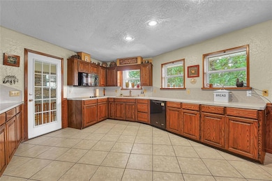 Kitchen with black appliances, a textured ceiling, a textured wall, light countertops, and brown cabinetry