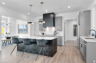 Kitchen with gray cabinetry, decorative light fixtures, a kitchen breakfast bar, a kitchen island, and light wood-style floors