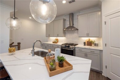 Kitchen featuring wall chimney exhaust hood, gas stove, a sink, gray cabinets, and light stone counters