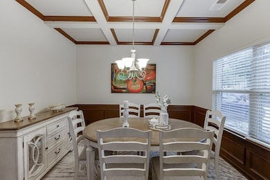 Dining area with plenty of natural light, coffered ceiling, a chandelier, beamed ceiling, and a wainscoted wall