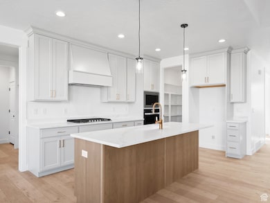 Kitchen featuring an island with sink, light wood-style flooring, light stone countertops, recessed lighting, and white cabinetry