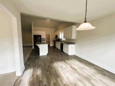 Kitchen with white cabinetry, lofted ceiling, dark countertops, dark wood-type flooring, and pendant lighting
