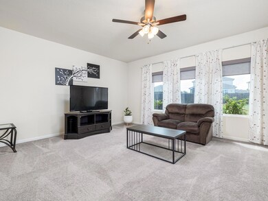 Carpeted living area with ceiling fan and baseboa