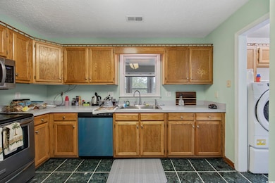 Kitchen featuring stainless steel appliances, a sink, light countertops, dark tile patterned flooring, and a textured ceiling