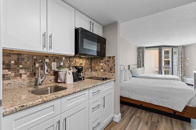 Kitchen featuring white cabinets, light stone countertops, decorative backsplash, black appliances, and dark wood-type flooring