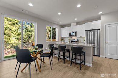 Stylish and functional, this open-concept kitchen features sleek quartz countertops, stainless steel appliances, and modern white cabinetry with ample storage. The center island with bar seating flows seamlessly into the dining space, highlighted by wide sliding glass doors that fill the room with natural light and create a perfect indoor-outdoor connection. Model Home pictured. Images may vary.