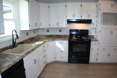 Kitchen featuring decorative backsplash, black appliances, white cabinetry, and dark countertops