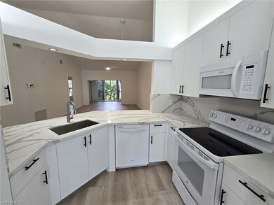 Kitchen featuring white appliances, light stone counters, white cabinetry, a peninsula, and light wood-style flooring