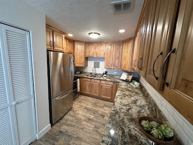 Kitchen with dark stone countertops, tasteful backsplash, stainless steel appliances, brown cabinetry, and dark wood-style flooring