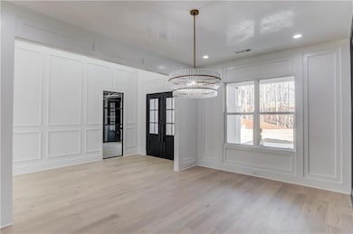 Unfurnished dining area featuring a decorative wall, light wood-style flooring, recessed lighting, and a chandelier
