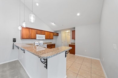 Kitchen featuring white appliances, a peninsula, brown cabinets, light stone counters, and high vaulted ceiling