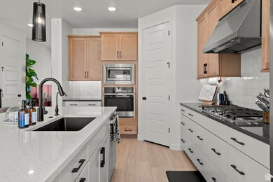 Kitchen with under cabinet range hood, stainless steel appliances, hanging light fixtures, recessed lighting, and light flooring