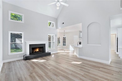 Unfurnished living room featuring high vaulted ceiling, light wood-type flooring, a brick fireplace, and ceiling fan