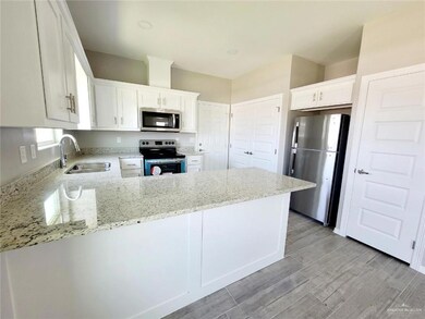 Kitchen with stainless steel appliances, light stone countertops, a peninsula, white cabinets, and light wood-style floors